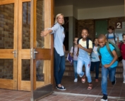 Teacher holding school door open and group of children running out.