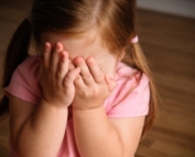 Little red-haired girl in pigtails covering her eyes in embarrassement.