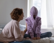 Mom talking with daughter who has her hoodie up over her head and pulled tight.