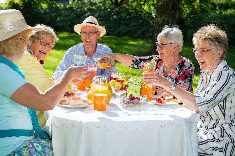 A group of elderly people sitting around a table, laughing and eating together.