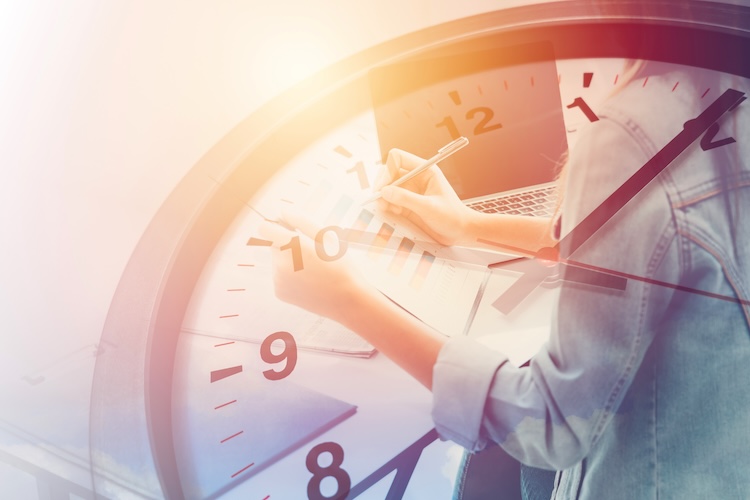Picture of busy person working on papers behind a big clock ticking away.