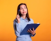 Woman thinking while holding a clipboard and pen.