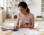 Smiling woman sitting at her desk working on taxes on her computer, surrounded by lots of paperwork.