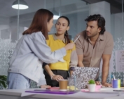 Three people looking at a computer and 1 is doing all the talking.