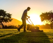 Man mowing the yard as the sun sets behind him.