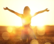 Woman in a field holding arms out to bright sunshine.
