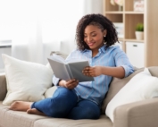 Young woman curled up on a sofa reading a book.
