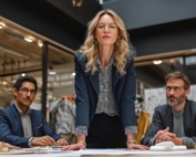 Adult professional woman standing to lead a meeting with other professionals.
