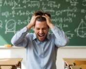 Frustrated teacher sitting in front of blackboard full of equations.