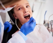 Child with braces sitting in dental chair while dentist looks at their teeth.